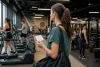 Une femme tenant une carte d’accès observe les équipements d’une salle de fitness fréquentée.