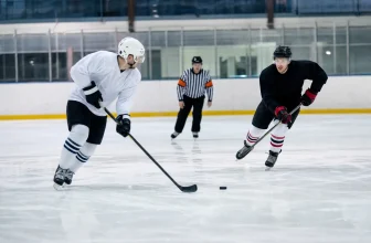 Deux hockeyeurs équipés patinent vers une rondelle sous le regard d’un arbitre.