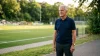 Homme âgé en polo bleu près d'un terrain de football
