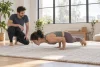 Une adulte travaille un appui d’elbow lever près du tapis sous le regard d’un coach.