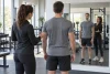 Un sportif et une coach observent sa posture générale devant un miroir en salle.