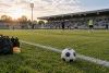 Des joueurs anonymes s’échauffent au loin sur un terrain de football sans identité de club.