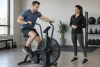 Adulte utilisant un air bike générique à intensité modérée sous le regard d’une coach.